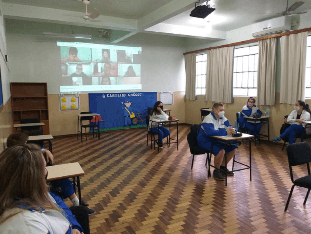 Iniciando ao ensino híbrido, com aulas acontecendo no formato presencial e virtual. As aulas estão sendo transmitidas ao vivo para os estudantes que estão em casa e todos podem participar em tempo real.