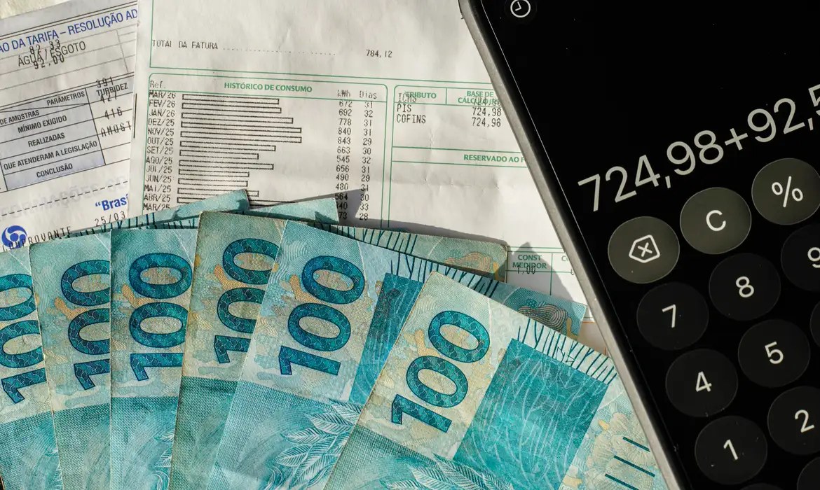 Notas fiscais e cédulas de cem reais sobre calculadora durante análise de documentos contábeis.