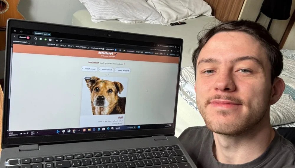 Homem apresenta plataforma digital de adoção de animais em tela de notebook, com imagem de cão exibida no site.