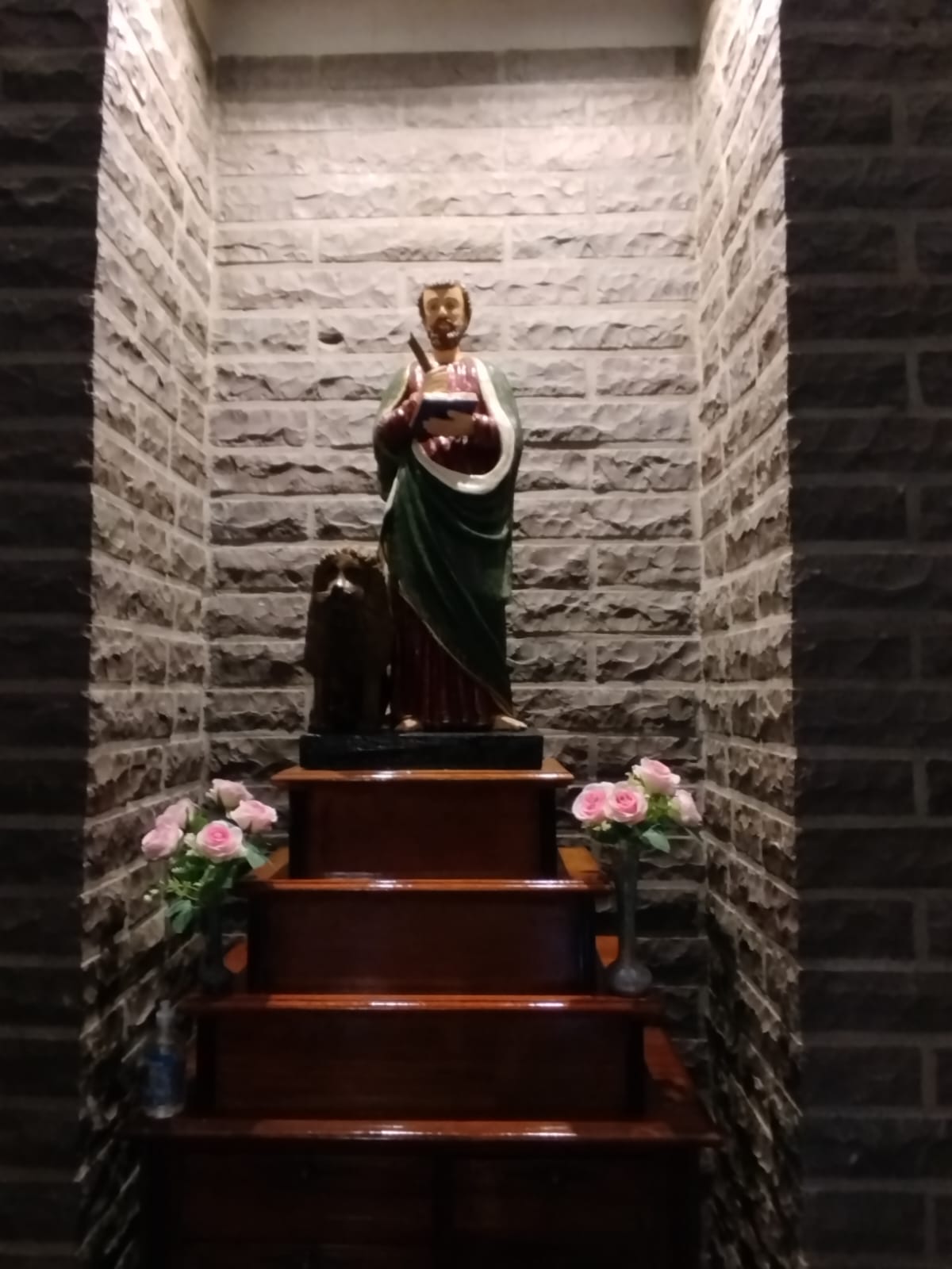 Estatua de São Marcos em capela da comunidade recebe flores cor-de-rosa durante preparativos para celebração do padroeiro.
