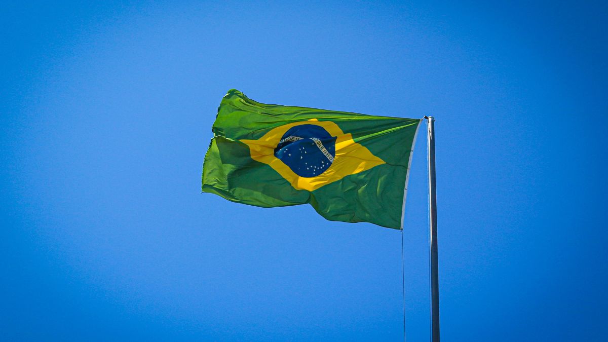 Bandeira brasileira tremula ao vento sob céu azul.