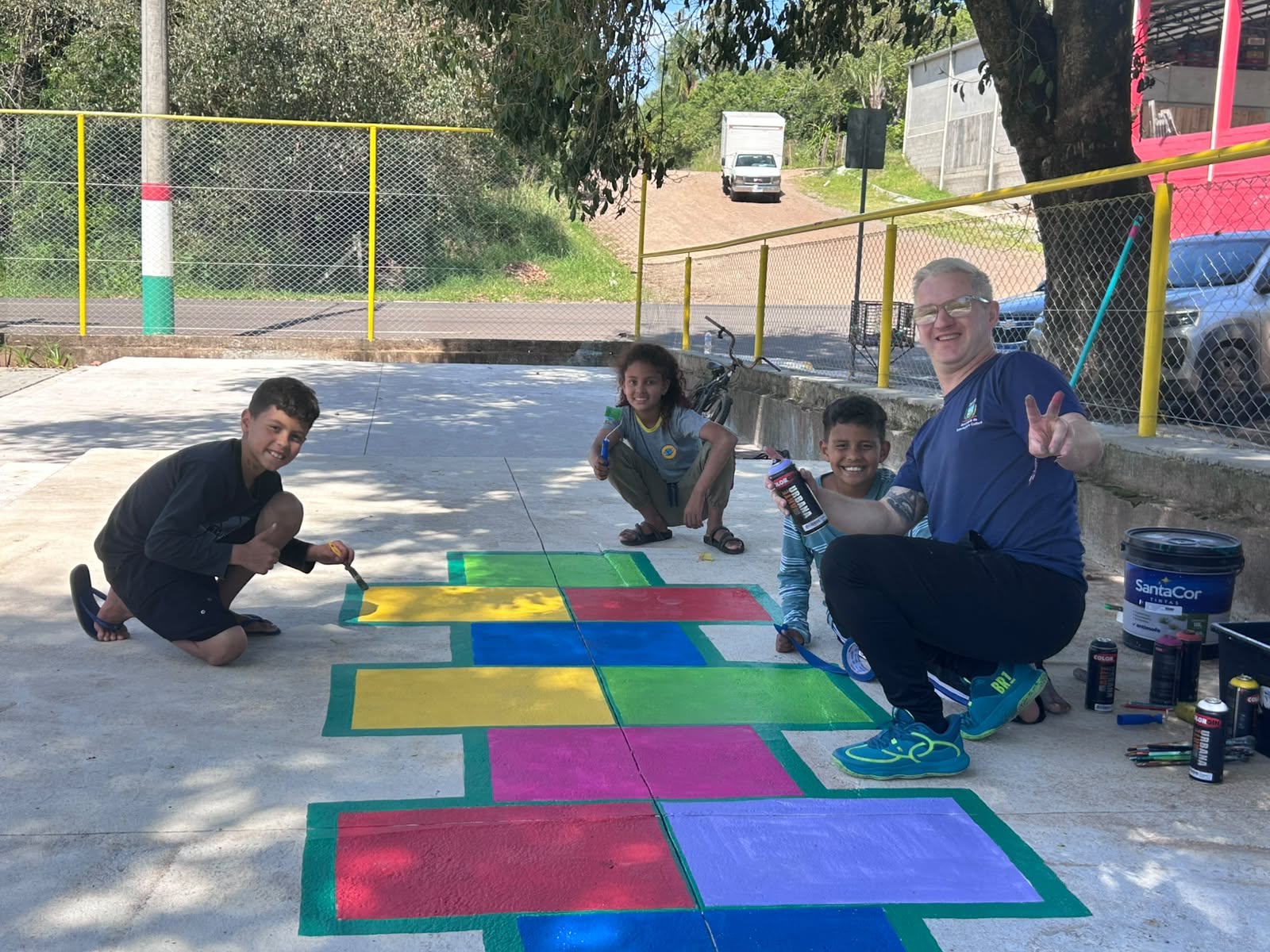 Crianças e servidor municipal posam junto a painel colorido recém-pintado na Praça Agostinho Costi, no bairro Planalto.