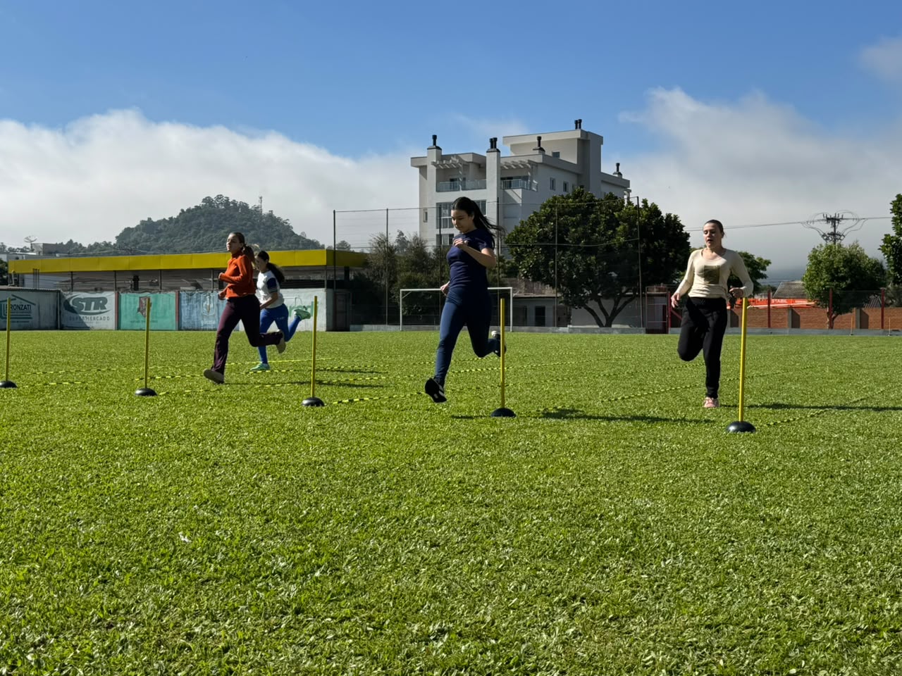 Estudantes participam de prova de atletismo nos Jogos Escolares Municipais em campo de futebol.