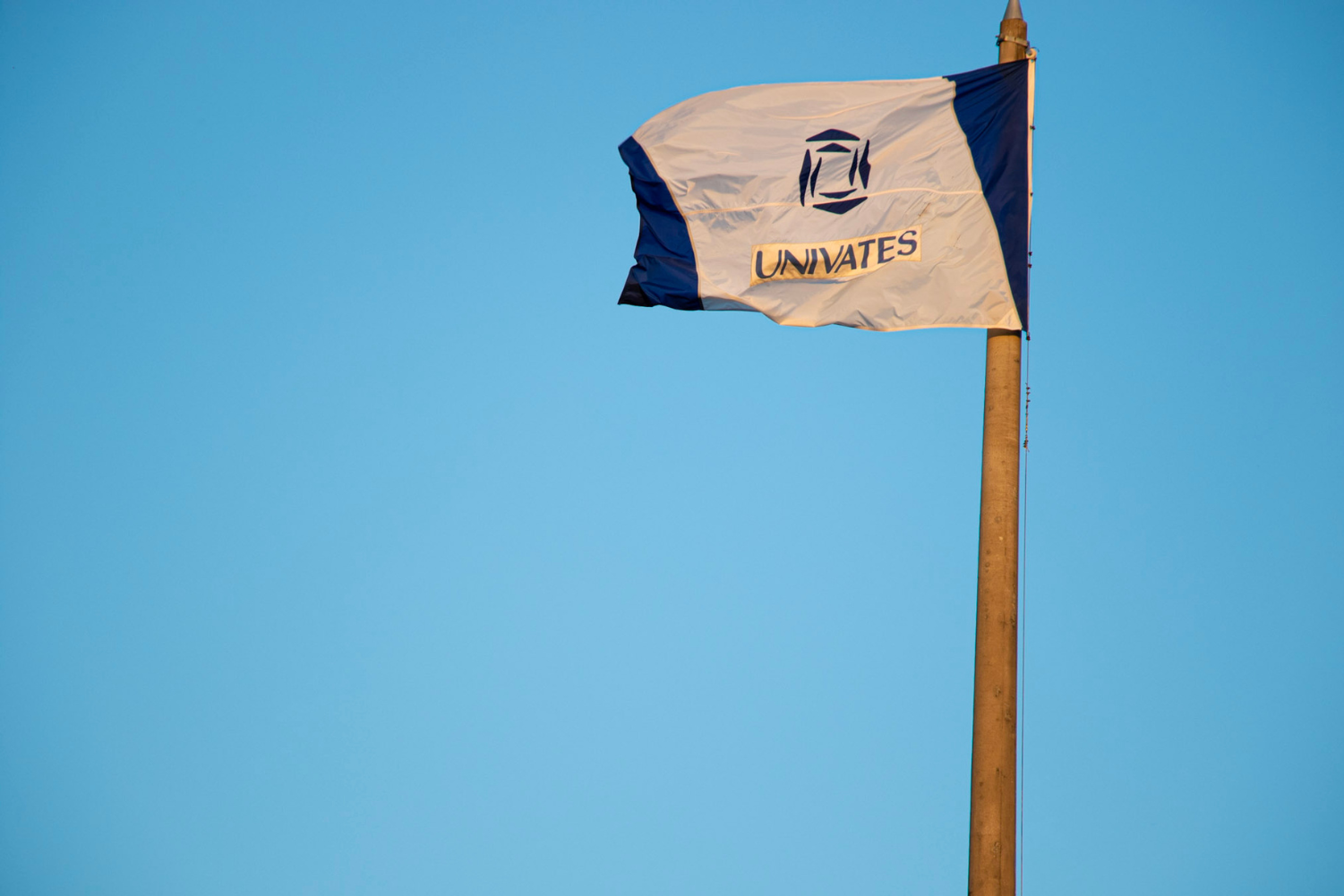 Bandeira da Univates tremula ao vento sob céu azul claro.