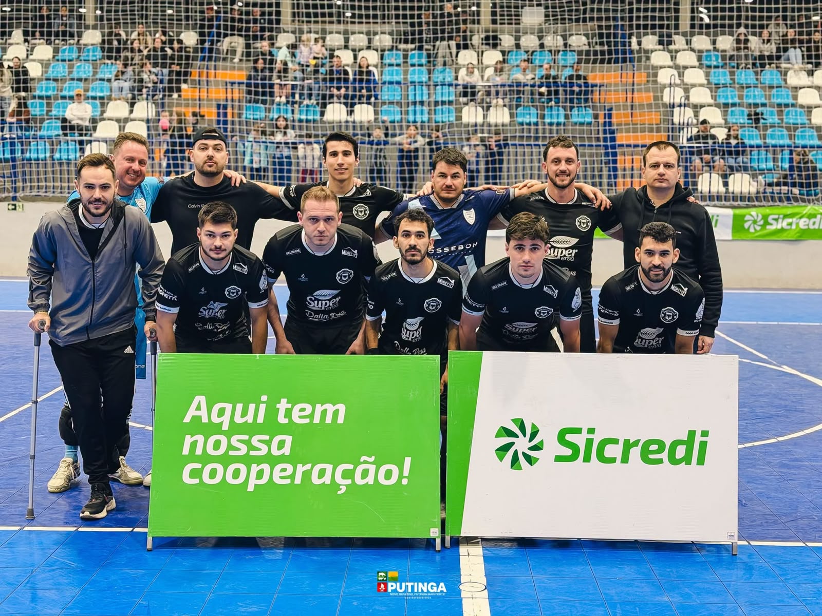 Equipes campeãs do Campeonato Municipal de Futsal de Putinga posam para foto na quadra com faixas de patrocínio.
