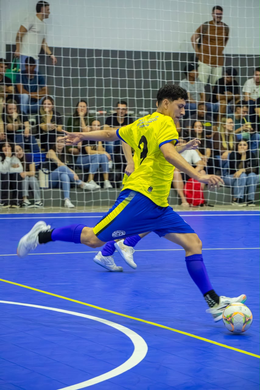 Atleta disputa bola durante partida de futsal no Ginásio do Centro Social Urbano de Roca Sales.