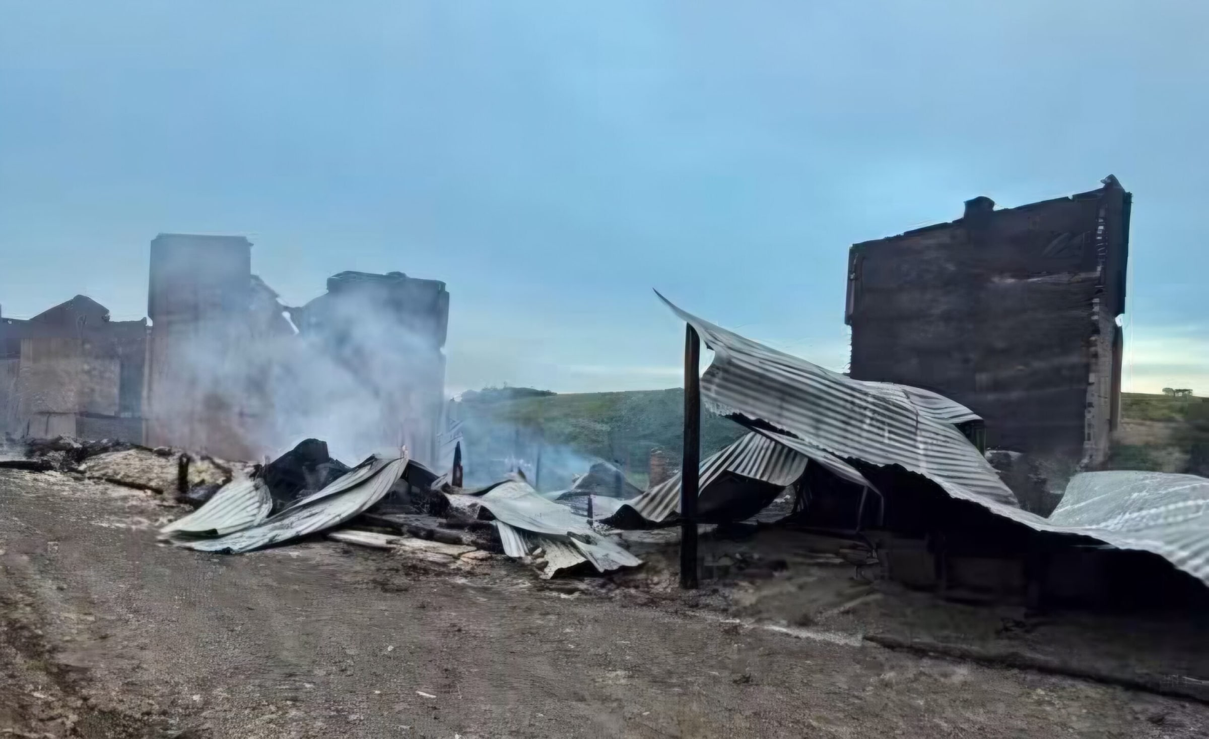 Estruturas de secagem de tabaco destruídas pelo incêndio em Boqueirão do Leão, com fumaça ainda saindo dos escombros.