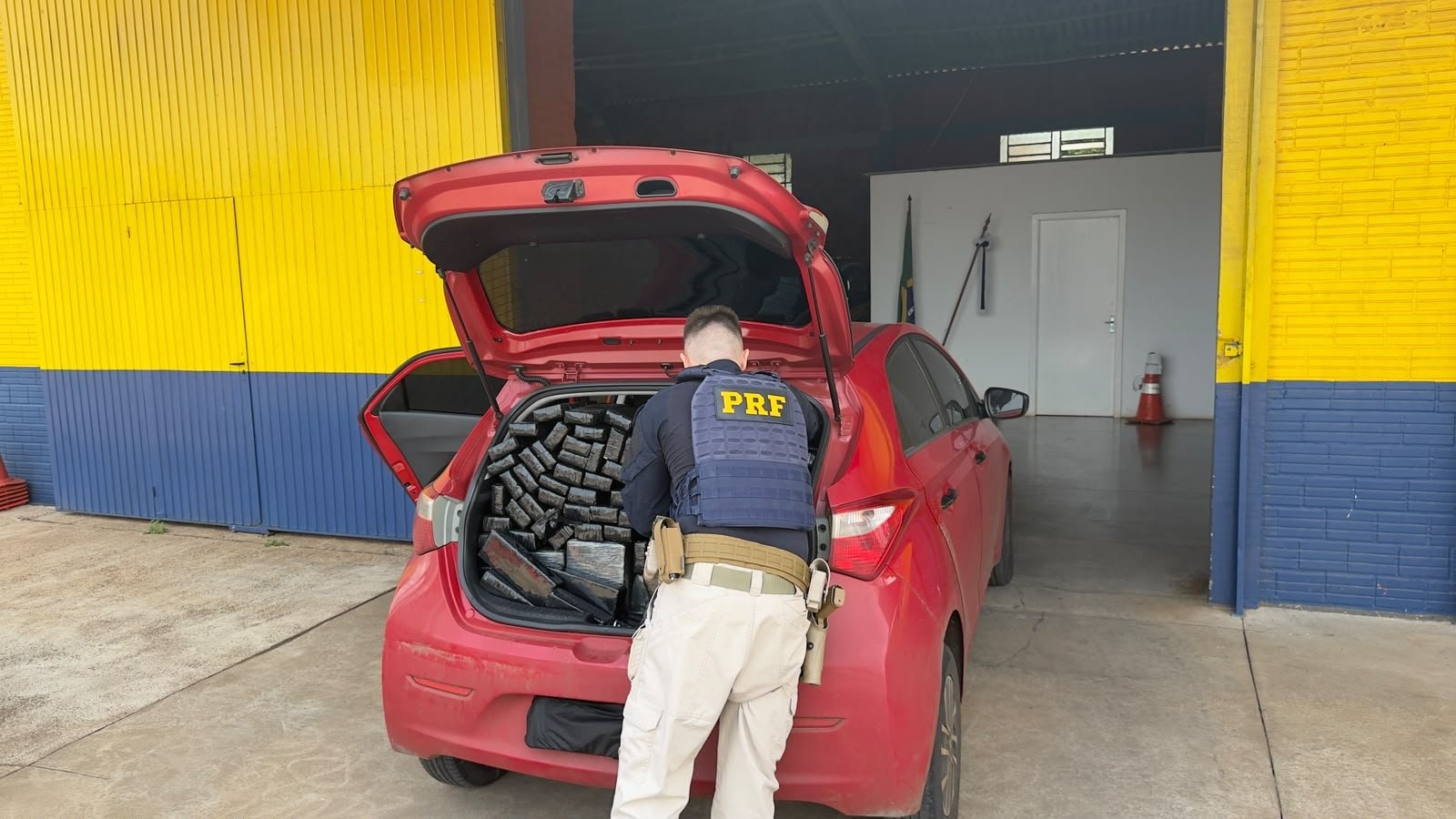 Policial da PRF inspeciona maconha apreendida no porta-malas de carro vermelho durante abordagem em Lajeado.