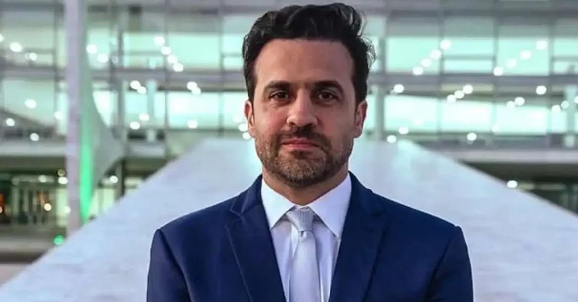 Homem de terno e gravata em ambiente de prédio moderno faz declaração sobre eleição presidencial.